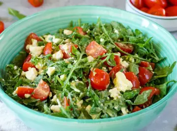 Frischer Rucolasalat mit saftigen Tomaten und cremigem Käse in einer türkisfarbenen Schüssel.