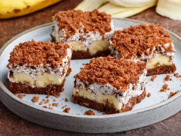 Vier Stücke saftiger Maulwurfkuchen vom Blech mit Bananen und Schokoladenstreuseln auf einem Teller.