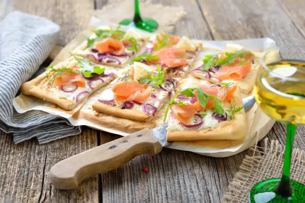 Flammkuchen mit Lachs und Crème fraîche, garniert mit Rucola und Dill, auf rustikalem Holztisch.