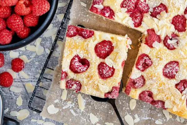 Schneller Kuchen mit gefrorenen Himbeeren, bestreut mit Puderzucker und Mandelblättchen. Ein Genuss für jeden Anlass!