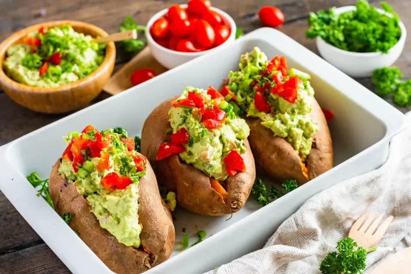 Gefüllte Süßkartoffeln mit Avocado-Topping. Leckere, kalte Rezepte mit Avocado, garniert mit Paprika und Kräutern.