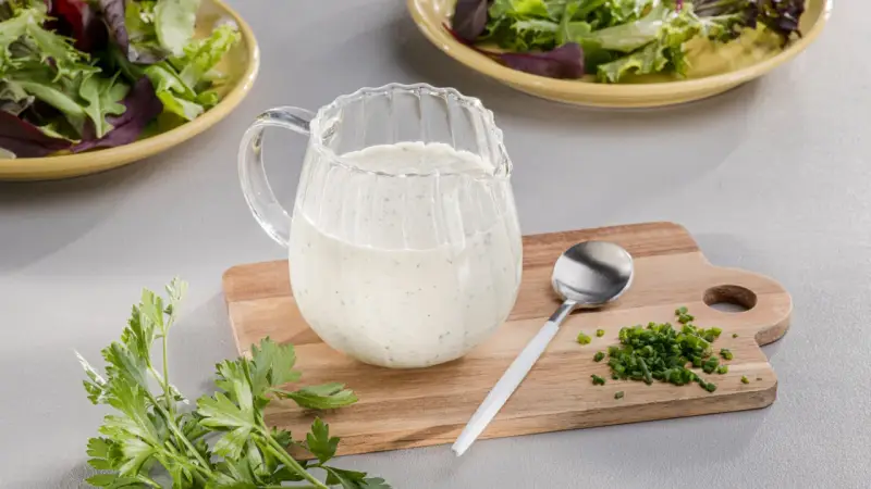 Ein Krug mit cremigem Ranch Dressing, daneben Schnittlauch und Petersilie. Perfekt für einen frischen Salat.
