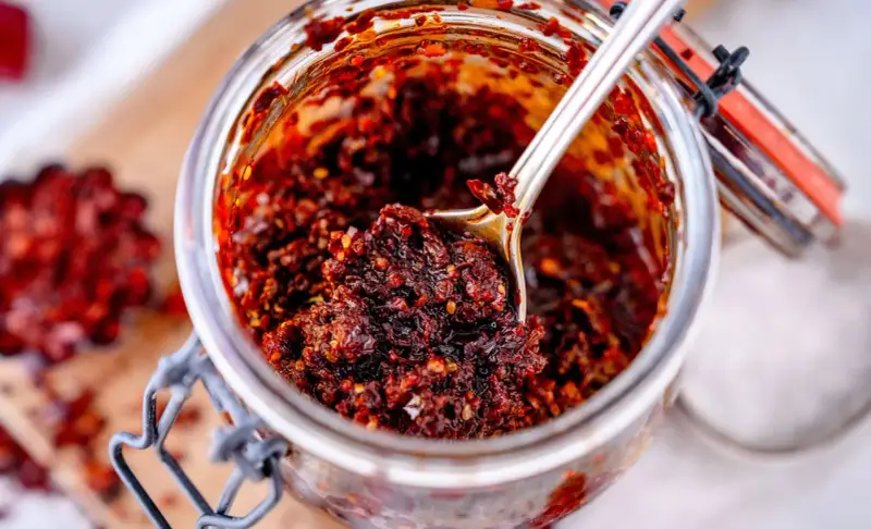 Ein Glas mit würzigem Chili Crunch, perfekt für jedes Chili Crunch Rezept. Eine Löffelspitze voller Geschmack!
