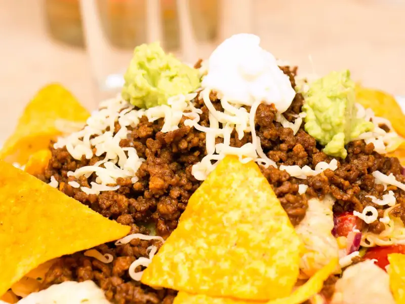 Schichtsalat mit Hackfleisch, Käse, Guacamole und saurer Sahne, garniert mit knusprigen Nachos.