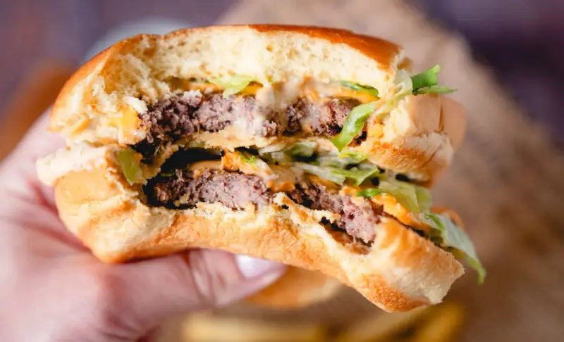 Ein saftiger Burger mit zwei Rindfleisch-Patties, Salat und der unverwechselbaren Big Mac Sauce, gehalten in einer Hand.