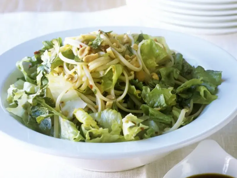 Ein leckerer Yum Yum Salat mit knackigem Eisbergsalat, Nudeln und Erdnüssen in einer weißen Schüssel.